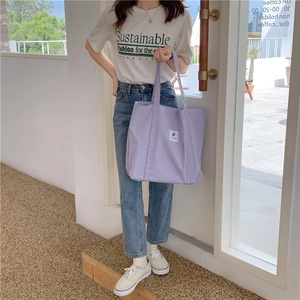 Close-up of a light purple canvas tote bag featuring a white square label and dual handles