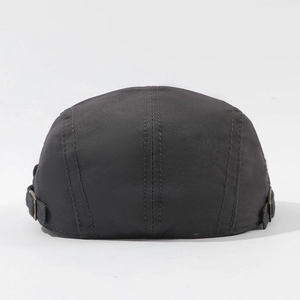 Detail of black cotton beret cap featuring adjustable bronze metal buckles on the back