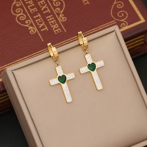 Golden cross earrings with green heart gems and crystals on a beige jewelry box