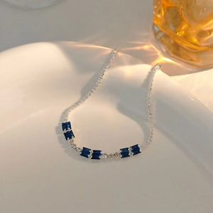 Detailed close-up of a silver tennis bracelet with blue gems on a white plate