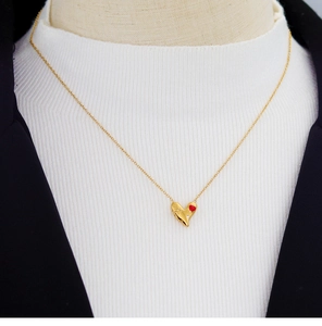 Pendentif cœur doré avec accent rouge porté sur un blazer noir et un haut blanc