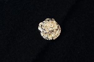 Macro shot of an irregular golden flower button on a black textured fabric background