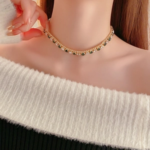 Close-up of gold necklace with alternating green and clear crystals worn by a model