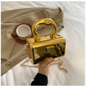 Detailed close-up of a metallic gold acrylic box bag with a unique heart-shaped handle