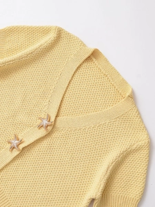 Detail of star-shaped gold buttons on yellow waffle knit sweater with V-neckline