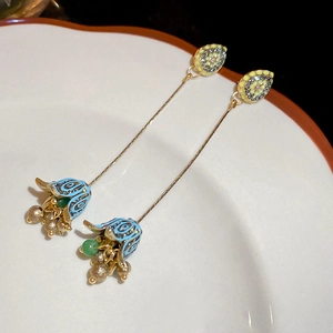 Macro shot of blue enamel flower earrings with gold tassel and green bead accents