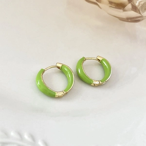 Detailed view of green enamel C-shaped hoop earrings with gold finish on ceramic texture