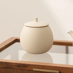 Minimalist beige ceramic tea canister with matte texture on wooden display stand