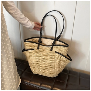Detail of straw woven tote bag featuring black leather handles on a brown leather bench