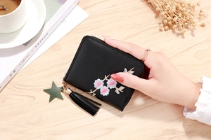 Close-up of black leather wallet with daisy embroidery, tassel, and star pendant