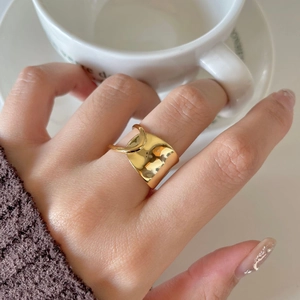 Detail of elegant gold wide overlapping ring worn by model holding a white coffee cup