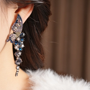 Détail de boucles d'oreilles ailes vintage avec zircons colorés et pompons