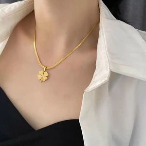 Detail of a gold clover pendant necklace on a model with a sleek snake bone chain