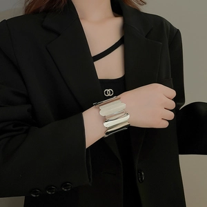Close-up of a wide silver cuff bracelet with vertical wave texture on a black suit sleeve