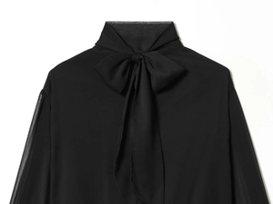 Detalle de blusa de gasa negra con cuello de lazo y tejido con textura de partículas