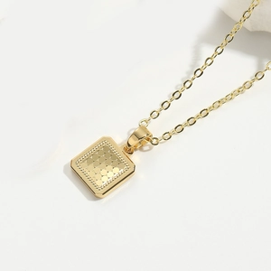 Macro shot of a gold square necklace pendant with circular relief texture and O-chain detail