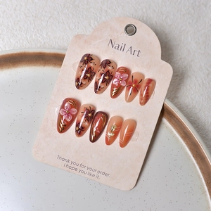 Macro shot of 3D pink flowers and gold leaf accents on almond-shaped press-on nails