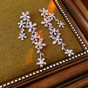 Macro view of silver flower tassel earrings with pink zircons on vintage fabric