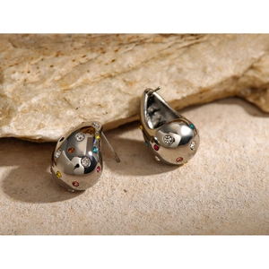 Macro shot of silver teardrop earrings with colorful rhinestones on natural rock background