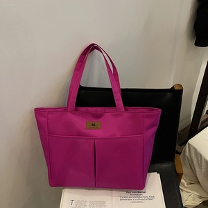 Vibrant magenta nylon tote bag with front pockets and top handles on a stylish black chair