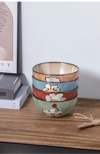 Stack of four colorful ceramic bowls with white floral patterns on a rustic wooden shelf
