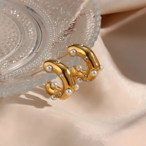 Macro view of gold C-shaped earrings with white pearls and sparkling zircons on satin