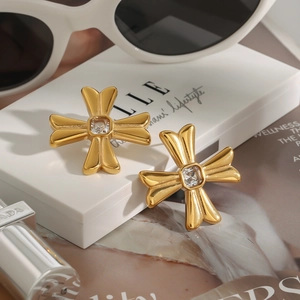 Macro detail of gold cross earrings with square zircon on ELLE magazine display