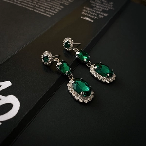 Macro detail of emerald green oval drop earrings with shimmering silver halo stones