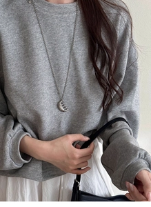 Close-up of a silver comb pendant necklace worn on a grey sweater with minimalist style