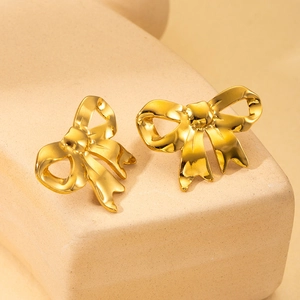 Detailed view of elegant gold bow stud earrings on a textured stone display base