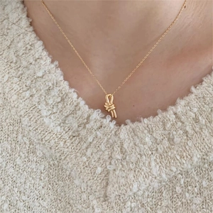 Minimalist gold knot pendant necklace in 925 sterling silver worn on a beige knit sweater