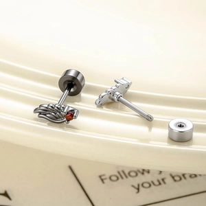 Cool angel wing cartilage studs with dark metal and red gemstone on beige surface