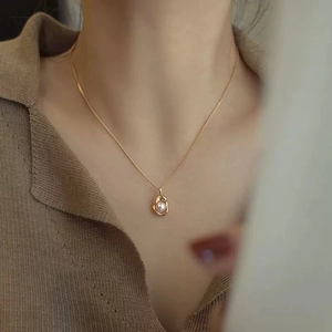 Detail of a golden pea necklace with a pearl pendant worn on a model's neck