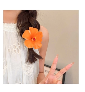 Detail of a bright orange hibiscus flower hair clip styled on a dark braided hairstyle