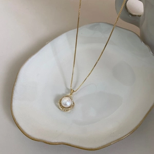 Detail of baroque pearl pendant with zircon inlay on a gold chain over ceramic plate