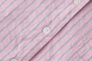 Détail de chemise rayée montrant la texture du tissu, les boutons et la couture de poche