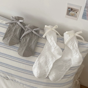 Gray and white knit socks with 3D bear pattern and bow details on a soft pillow