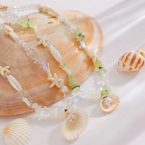 Detail of seashell and pearl necklace with light green crystals on large shell background