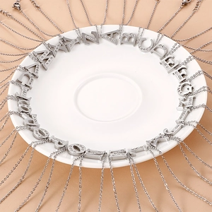 Silver A-Z letter pendant necklaces with rhinestones arranged on a white ceramic plate