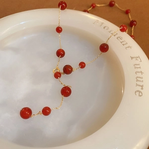 Detail of red agate beaded Y-necklace with gold plated chain on white ceramic plate