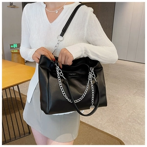 Detail of black pebbled leather tote bag featuring silver chain straps and metallic charms
