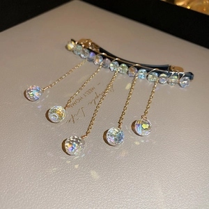 Close-up of golden tassel hair clip with crystal beads on a premium display base