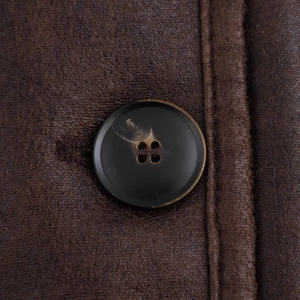 Macro detail of black button on brown leather jacket with durable stitching