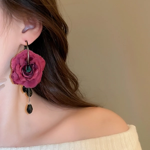 Detail of red fabric rose earrings with black beads and tassels on a model