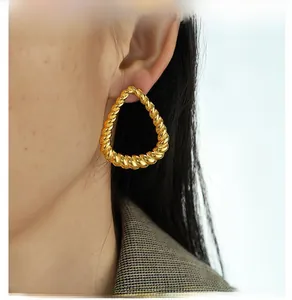 Close-up of chunky gold teardrop earrings with twisted rope texture on a model