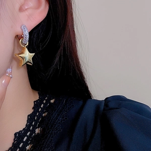 Detailed view of dangling gold star pendant with micro-pave crystals on silver hoop earring