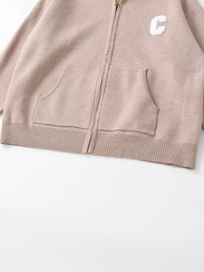 Detail of khaki knitted hoodie showing metal zipper pockets and ribbed hem with letter C