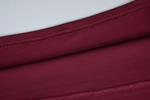 Dettaglio macro del tessuto a maglia bordeaux scuro con cuciture taglia-cuci