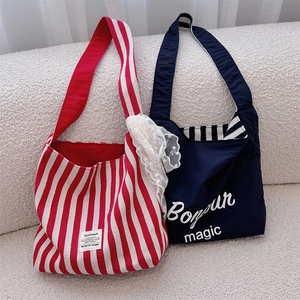 Close-up of red striped canvas tote with lace and navy blue bag on white sofa