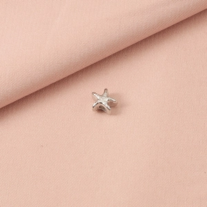 Macro-opname van een zilveren zeesterkraal voor sieraden op roze stoffen achtergrond